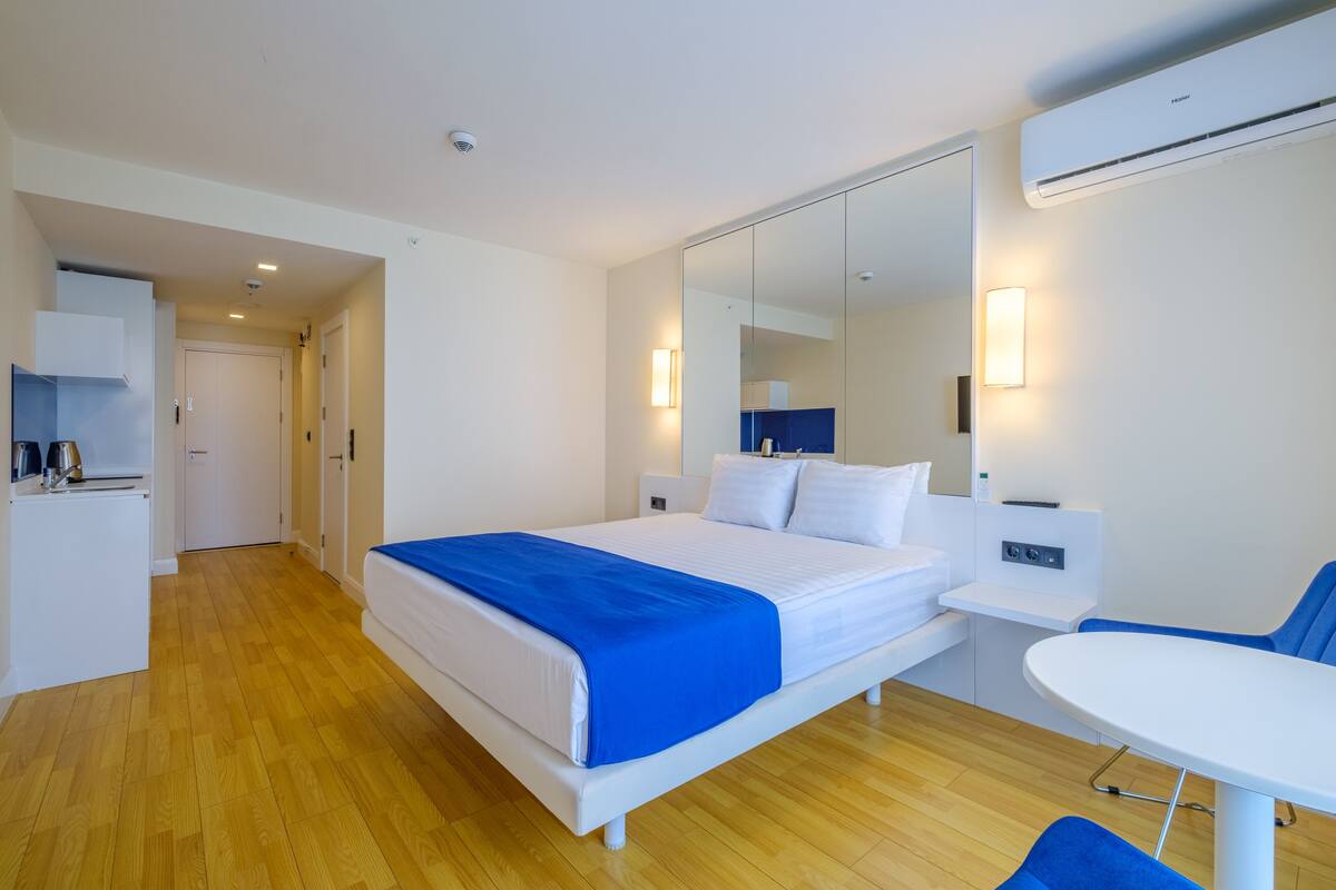 Una habitación de hotel moderna con cama, mesita de noche y una pequeña zona de escritorio.