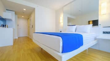 Una habitación de hotel moderna con una cama grande, una mesita de noche, un espejo y un armario.