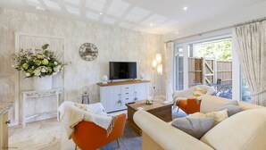A living room with a TV, sofa, and coffee table, a decorative clock, and a flower arrangement.