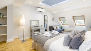 A modern bedroom with a skylight, a bedside table, a large bed with pillows, and a dresser with a mirror.