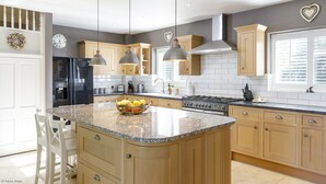 A modern kitchen with granite countertops, wooden cabinets, a central island, pendant lighting, and a built-in oven.
