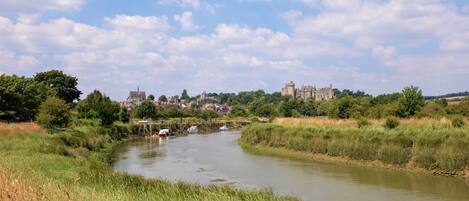 Une rivière où naviguent des bateaux, bordée de verdure et avec un bâtiment historique visible au loin.