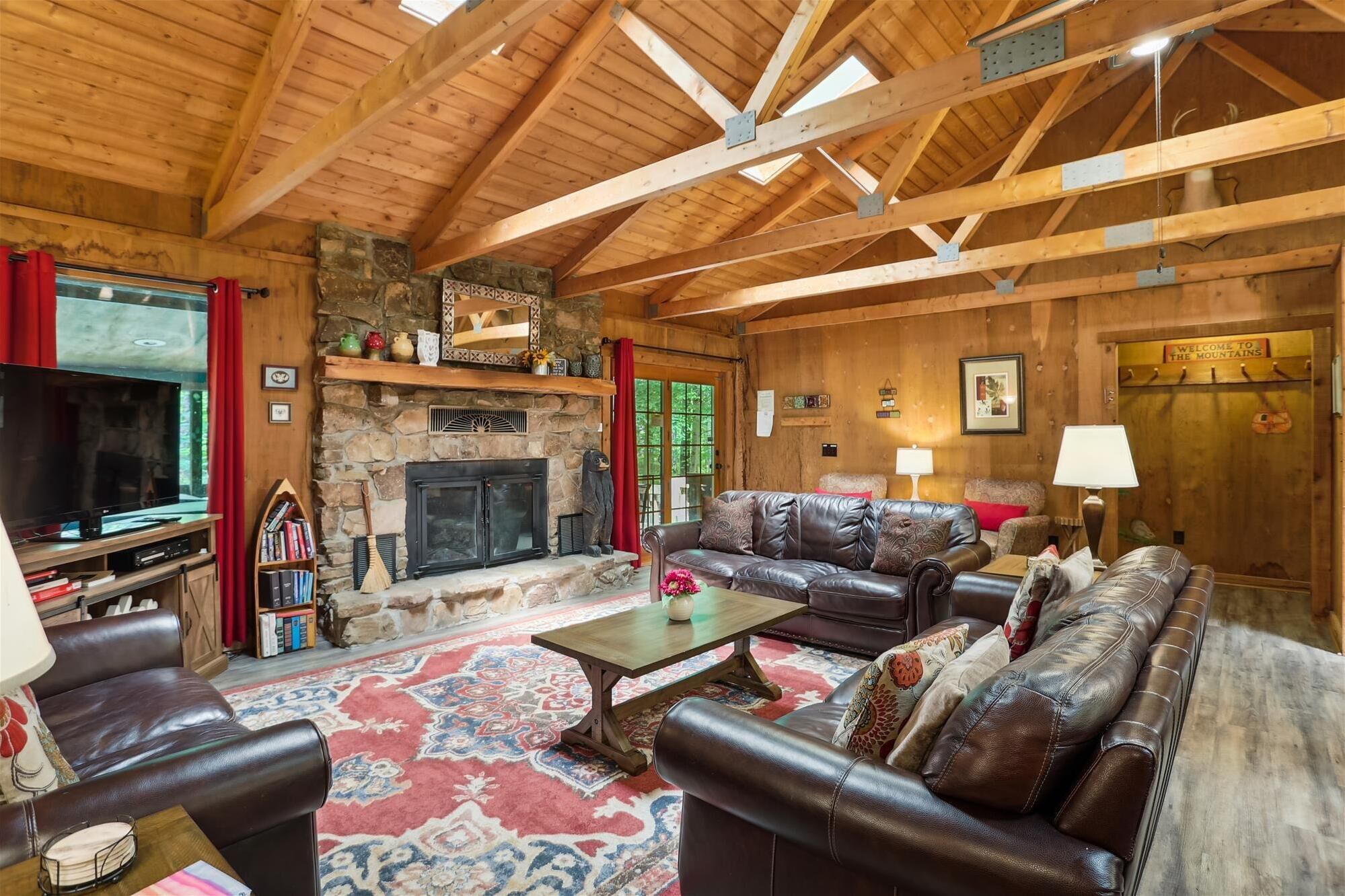 A cozy log cabin interior with a stone fireplace, leather sofas, and a television.