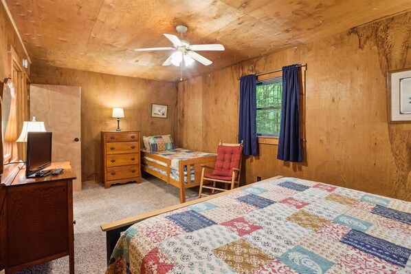 A cozy wooden room with a bed, a desk with a laptop, a chair, a dresser, and a ceiling fan.