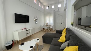 A modern living room with a grey sofa, white side table, and a flat-screen TV mounted on the wall. - 2 Bedroom Villa With Heated Pool (Torre-Pacheco)