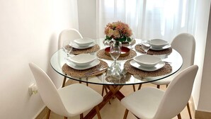 A round glass dining table with white chairs, set with plates, glasses, and a vase of flowers. - 2 Bedroom Villa With Heated Pool (Torre-Pacheco)