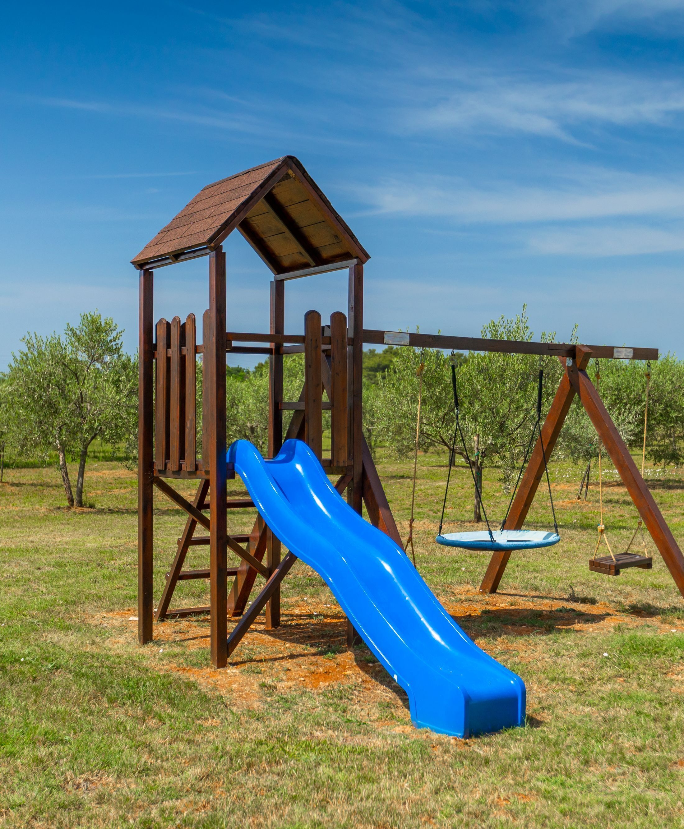 A wooden playground structure with a slide and swings in a grassy field.