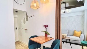Una cocina moderna con suelo de madera, una mesa de comedor con sillas, luces colgantes y vistas a un salón con un sofá y una mesa de centro.