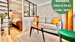 Una sala de estar moderna con un sofá, una mesa de centro y un sillón verde. Se ve una escalera a la izquierda y un espejo grande en la pared.