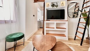 Una sala de estar moderna con un mueble de televisión de madera, un taburete acolchado verde y una mesa de madera.