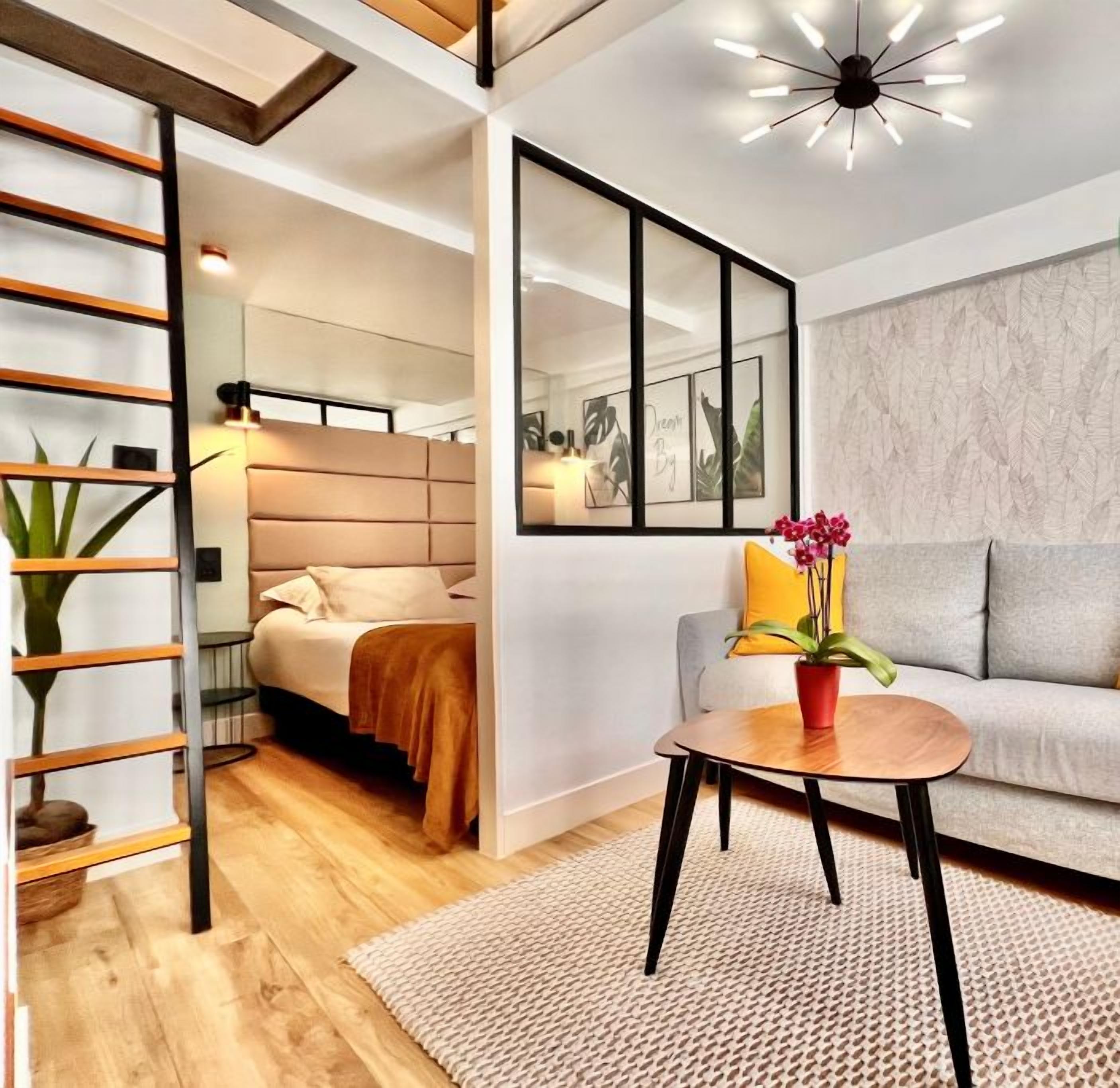 Ein modernes Wohnzimmer mit einer Couch, einem Couchtisch und einem grünen Sessel. Eine Treppe befindet sich links und ein großes Spiegel hängt an der Wand.