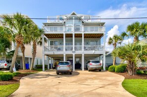 A two-story building with a covered parking area, palm trees, and a clear sky.