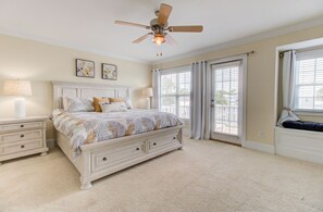 A bedroom with a bed, nightstands, a ceiling fan, and large windows. -  🌹Beach Rose: Multiple Decks | Walk to Beach Access | Ocean Views🌹 (Carolina Beach)