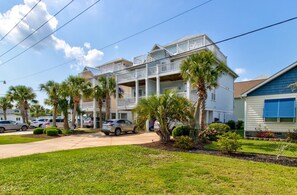 A multi-story residential building with balconies, parked cars, and palm trees. - 🌹Beach Rose: Multiple Decks | Walk to Beach Access | Ocean Views🌹 (Carolina Beach)