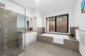Une salle de bain moderne dotée d’une douche à parois de verre, d’une baignoire sur pieds et d’une fenêtre avec stores.