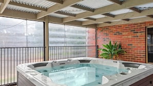 Een jacuzzi in een overdekte buitenruimte met een bakstenen muur en een plant.