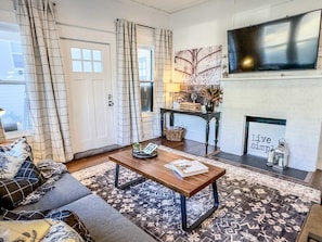 A living room with a sofa, a coffee table, a fireplace, and a television. - *Magnolia Masterpiece* | Family Gathering Place (Waco)