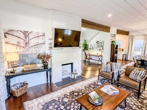 A spacious living area with a fireplace, a television mounted on the wall, and a dining area with a table and chairs. - *Magnolia Masterpiece* | Family Gathering Place (Waco)