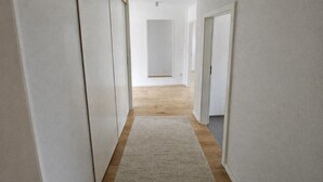 Ein schmaler Flur mit weißen Wänden und Holzboden, der zu einer Tür am Ende führt.