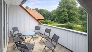 Ein Balkon mit rundem Tisch und sechs Stühlen, mit Blick auf eine grüne Landschaft mit Bäumen und einem Haus.