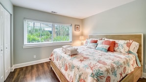 A bedroom with a large bed, a window with blinds, a bedside lamp, and a framed picture on the wall. - Sunset Rentals | Island House 125 | Dog Friendly (Hilton Head Island)
