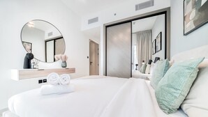 A modern hotel room with a large bed, a round mirror, a wardrobe, and a vanity with a mirror. - Polished 1BR at Binghatti Creek Al Jadaf by Deluxe Holiday Homes (Dubai)