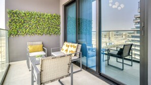 A balcony with wicker furniture, a glass table, and a green wall decoration. - Polished 1BR at Binghatti Creek Al Jadaf by Deluxe Holiday Homes (Dubai)