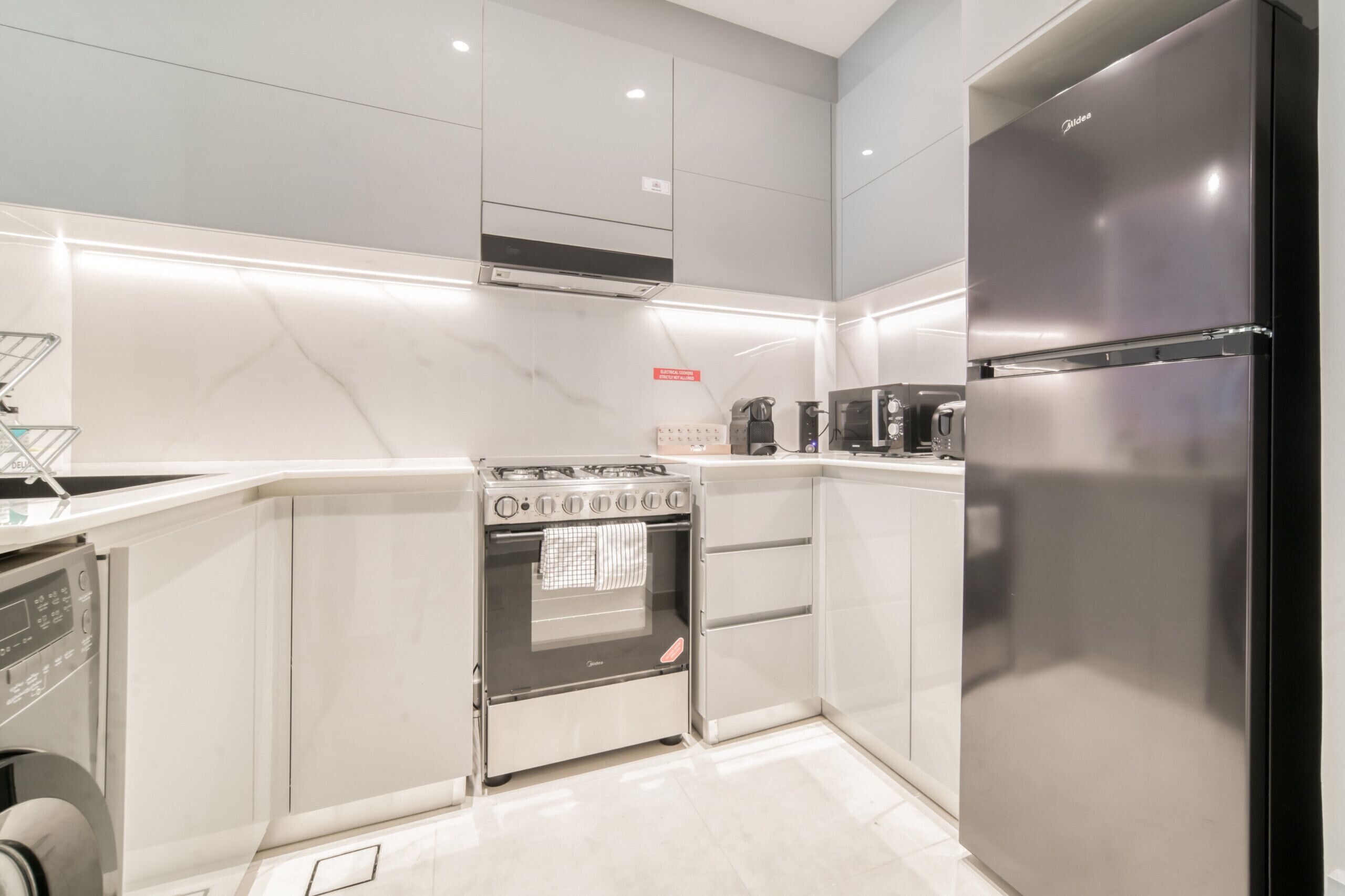 A modern kitchen with a built-in oven, a stainless steel refrigerator, and a coffee machine.