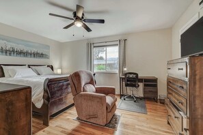 Un dormitorio con una cama, un sillón reclinable, un escritorio, una silla, un aparador y un ventilador de techo.