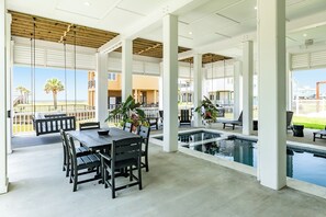 Un espacio al aire libre techado con piscina, asientos y vistas a la playa.