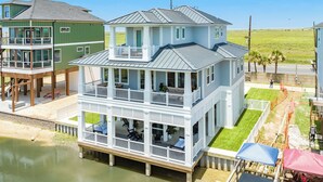 Une maison à deux étages située au bord de l’eau, dotée d’un balcon, d’une terrasse couverte et offrant une vue sur l’eau.