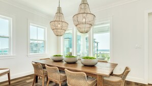 Un coin repas avec une table en bois, des chaises en osier et deux grands lustres.