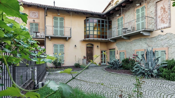 Ein Innenhof mit Kopfsteinpflasterwegen, grünen Fensterläden und einem zentralen Gebäude mit einer Holztür und Fenstern.