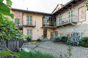 A courtyard with cobblestone paths, green shutters, and a central building with a wooden door and windows. - Residenza Isolina (Monforte d'Alba)
