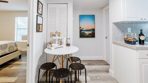 A compact kitchen with white cabinets, a dining table with four chairs, and a small island with a basket and bottles. - Cozy House /MarlinsStadium/ Brickell / Beach / Airport / Port Cruise /Pets (Miami)