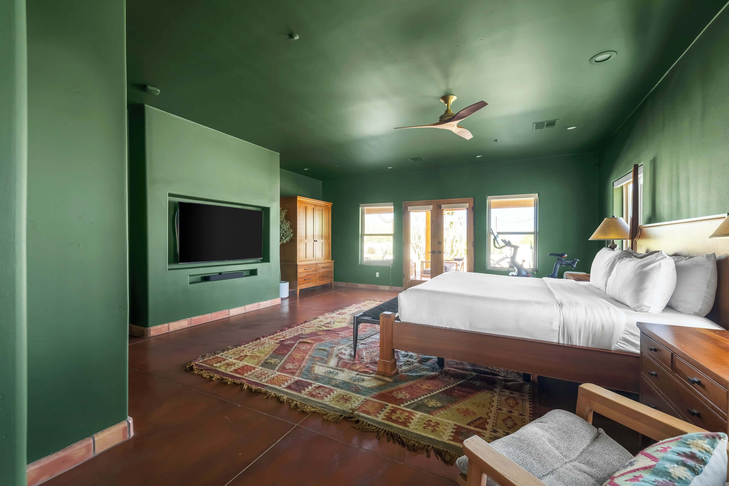 A bedroom with a large bed, a ceiling fan, a TV, and a window.