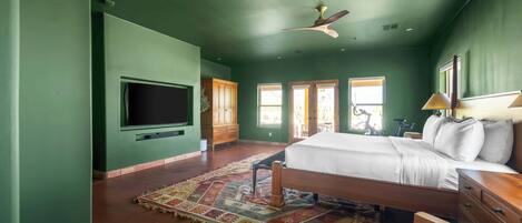A bedroom with a large bed, a ceiling fan, a TV, and a window.
