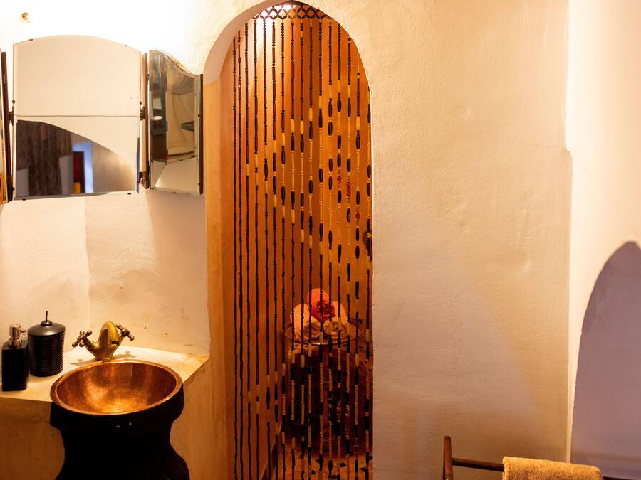 A bathroom with a wooden slatted partition, a copper basin, and a mirror above it.