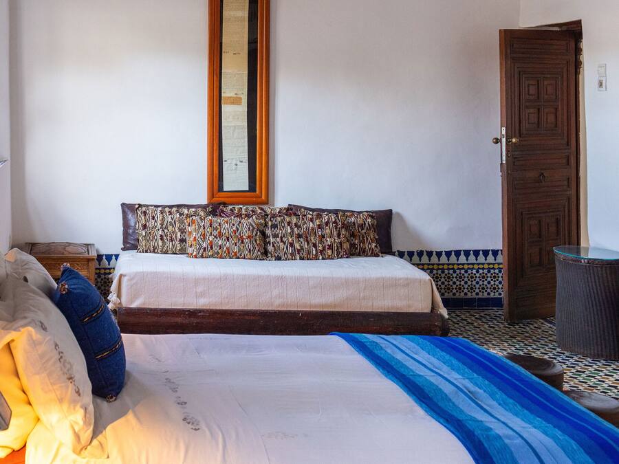 A bedroom with two beds, a wooden door, a trash bin, and a wall-mounted air conditioner.