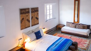 A bedroom with a large bed, a smaller bed, a window, a mirror, and a patterned rug. - Riad 9 Fez  (Fes)