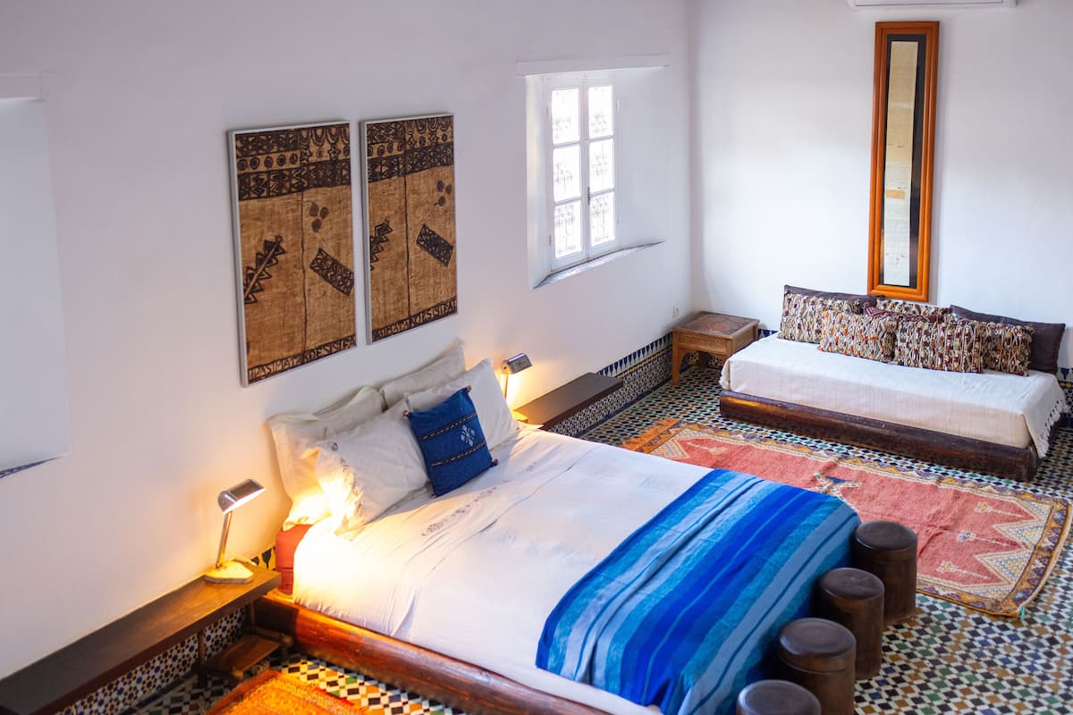Un dormitorio con una cama grande, una cama más pequeña, una ventana, un espejo y un tapete estampado.