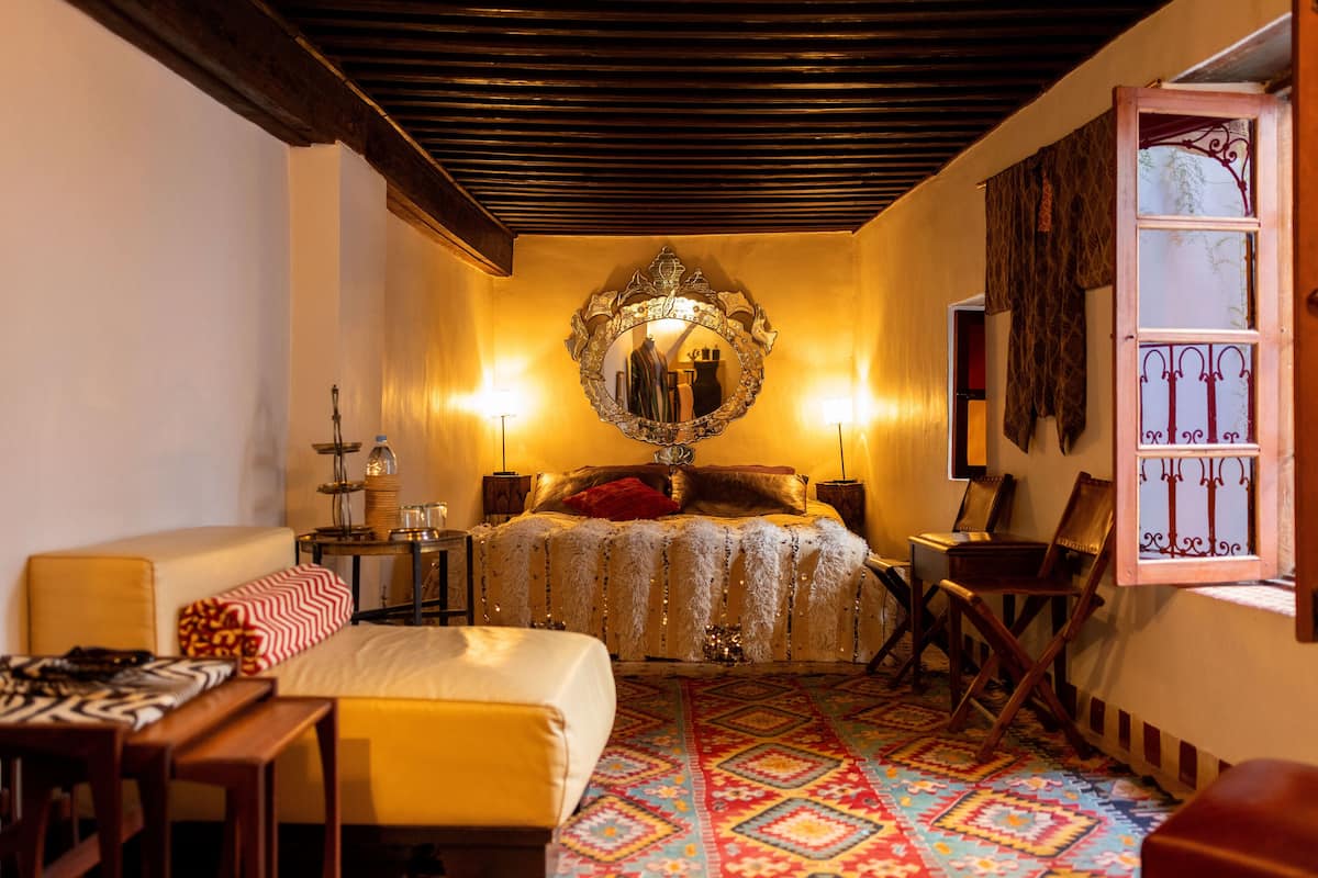 Una habitación de hotel con cama, escritorio, silla, espejo y ventana con cortinas.