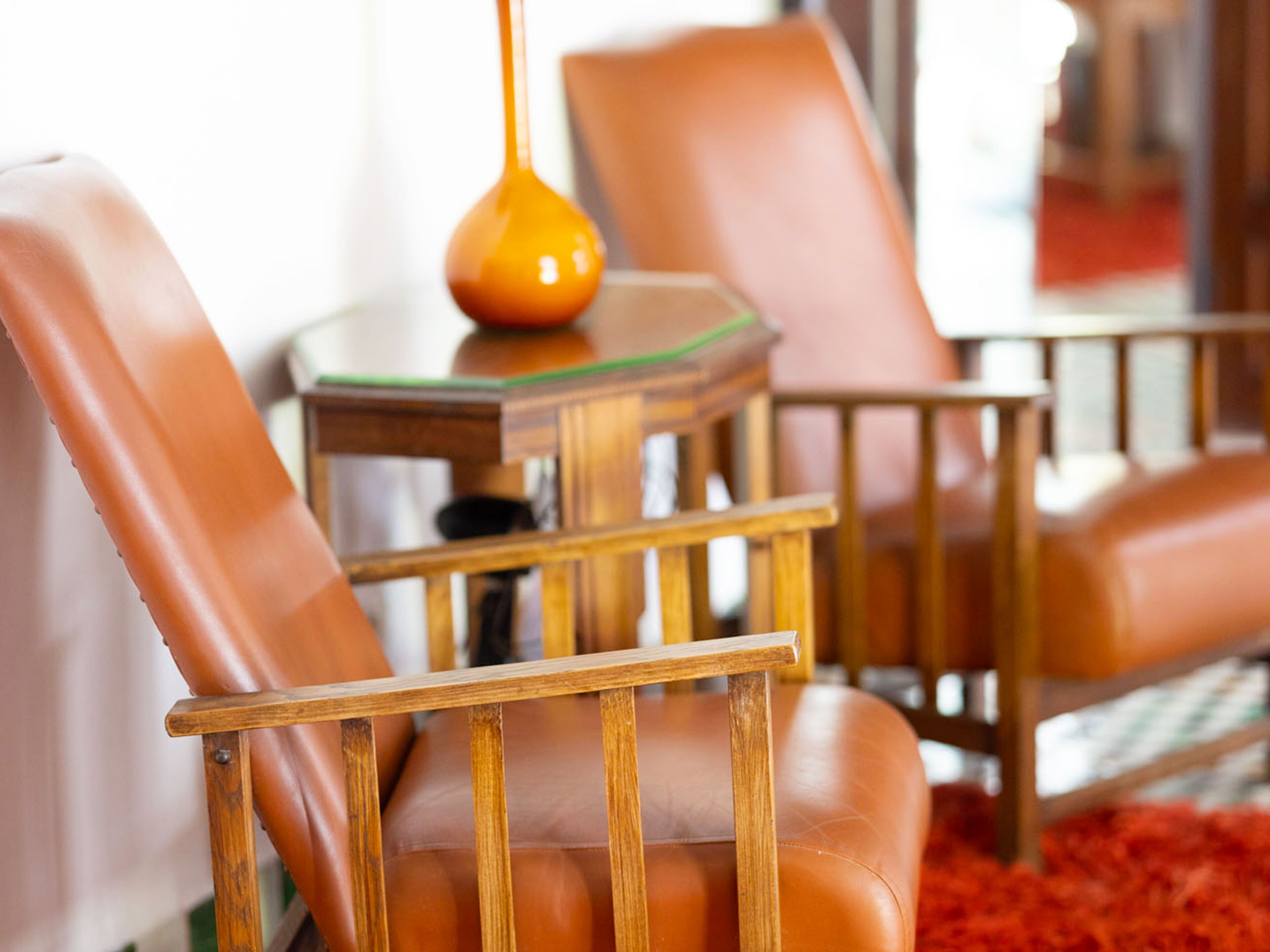 Una sala de estar moderna con sillones de cuero, una mesa de centro de madera y una mesa con cubierta de vidrio y una lámpara amarilla.