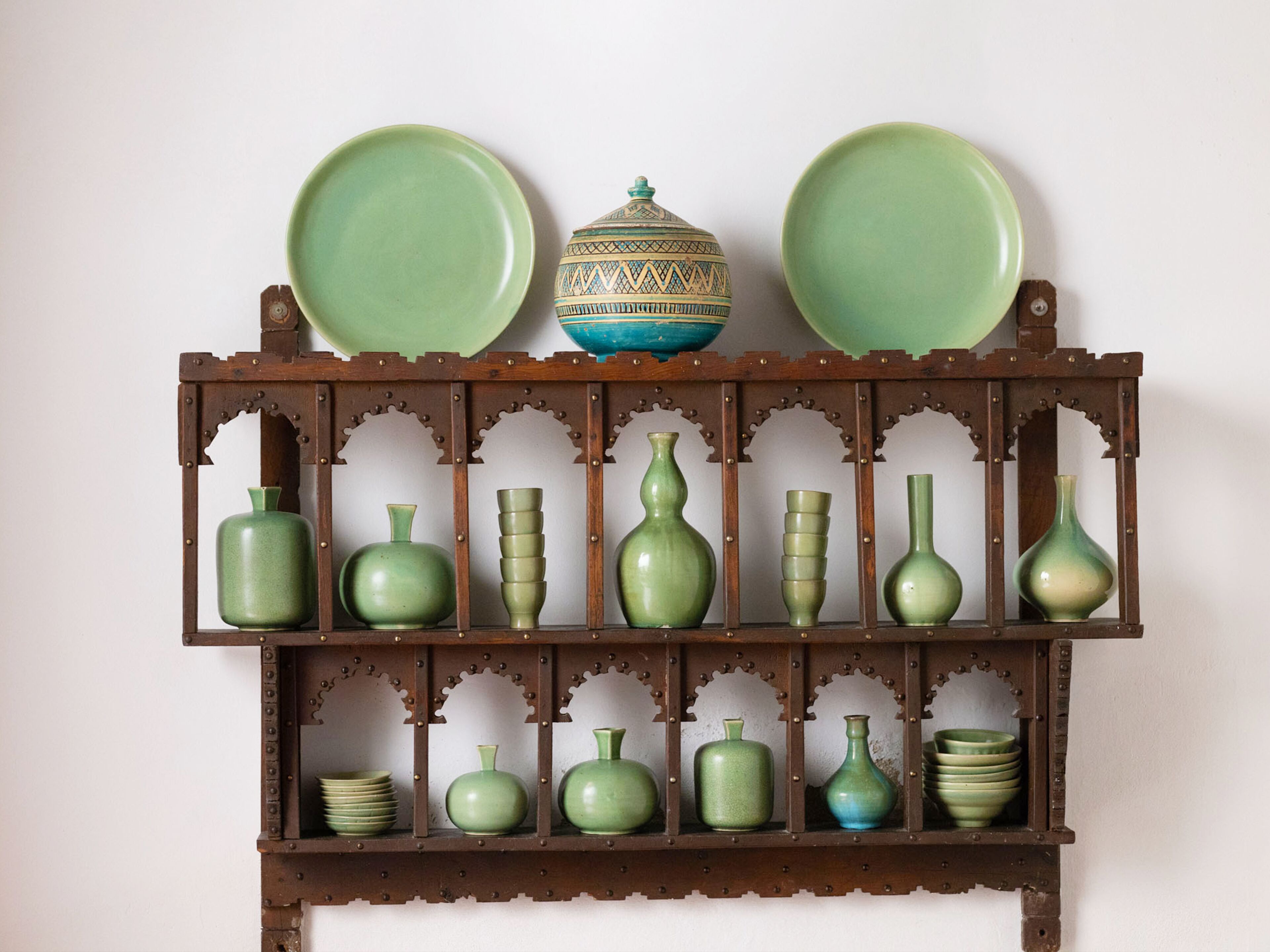 A wooden shelf with various green ceramic items, including plates, bowls, and vases.