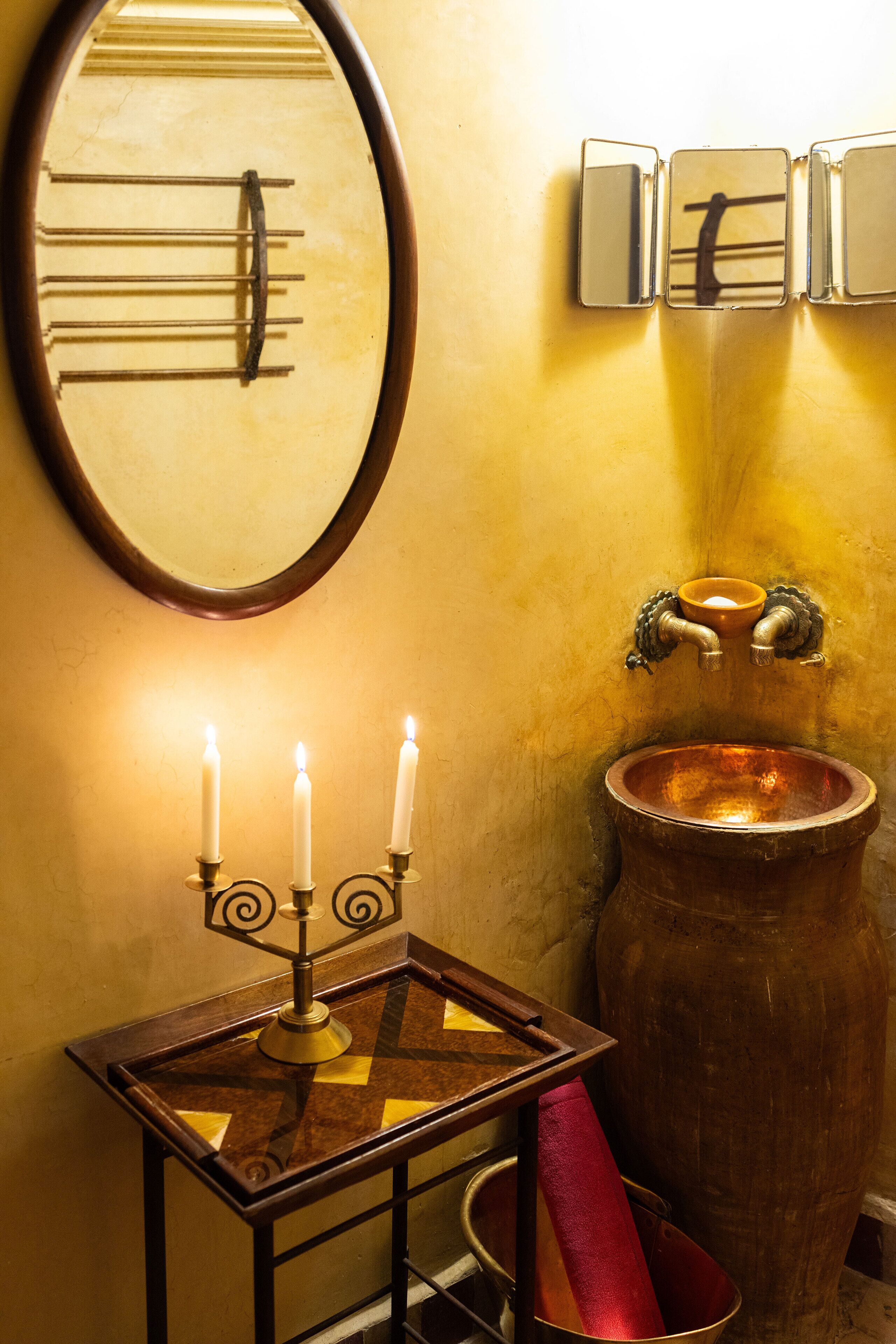 A bathroom with a mirror, a sink with a copper basin, and a candle holder with three candles.