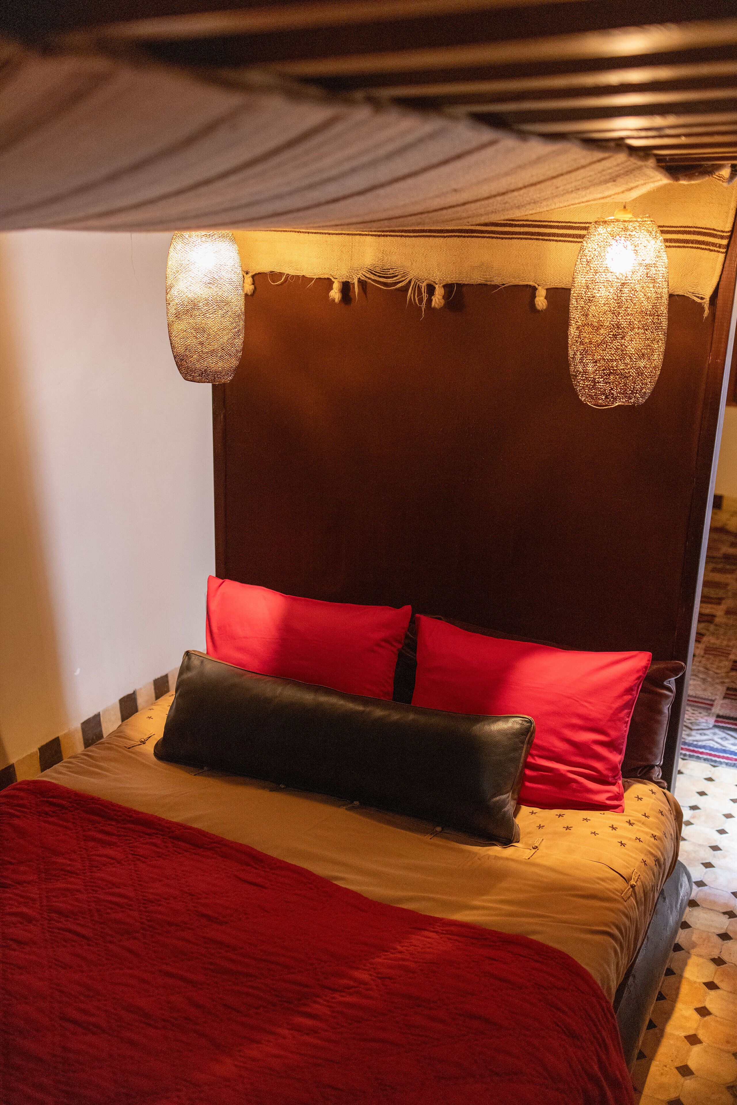 Un lit avec une tête de lit rouge et noire, une couverture rouge et deux luminaires suspendus.