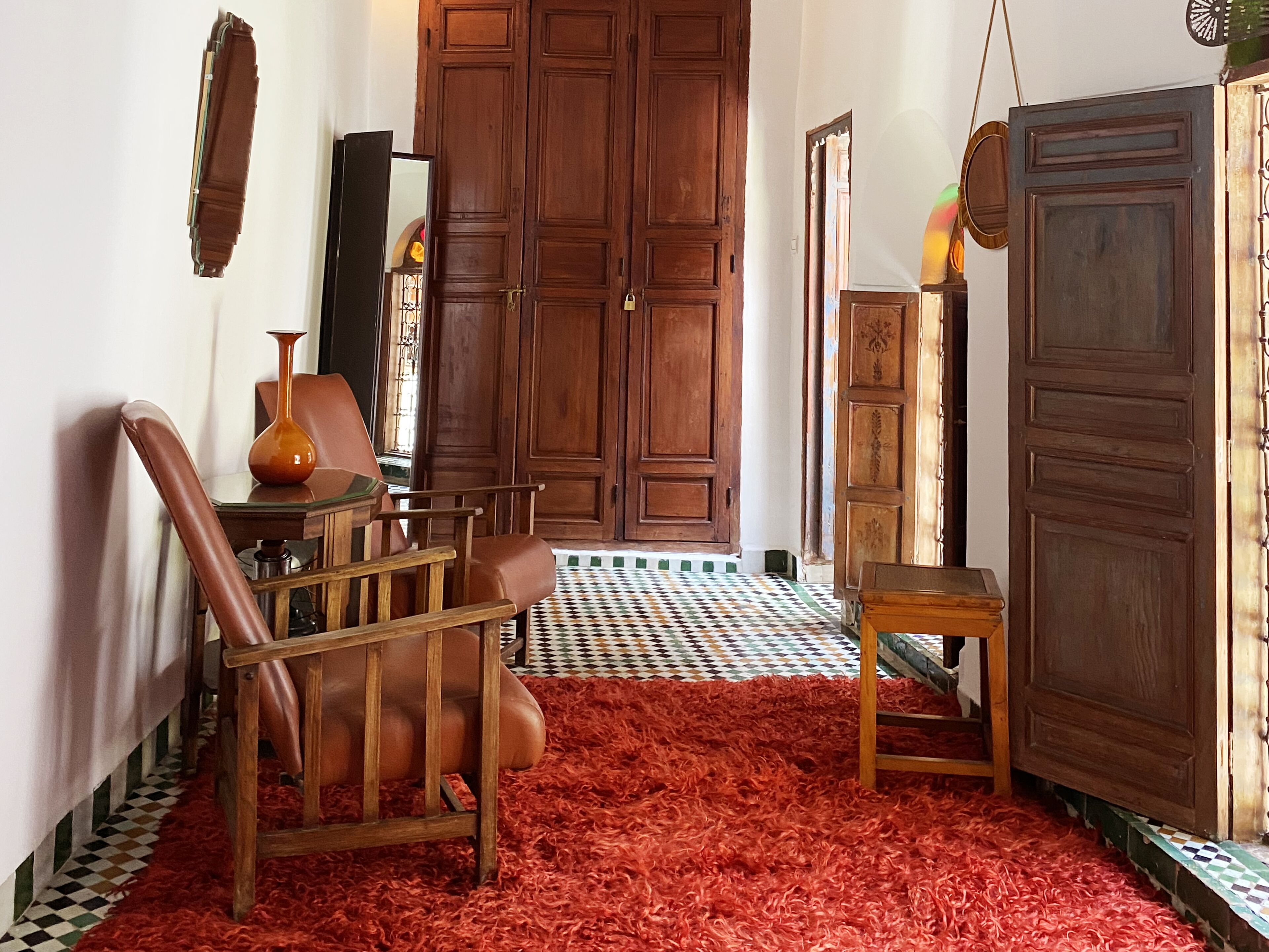 Una habitación con piso a cuadros, alfombra de pelo rojo, muebles de madera y una gran puerta de madera.