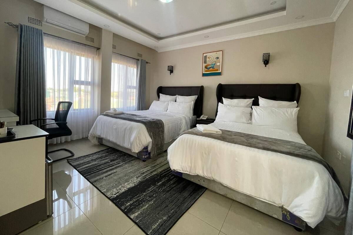 Quarto de hotel com duas camas, uma escrivaninha e uma cadeira.
