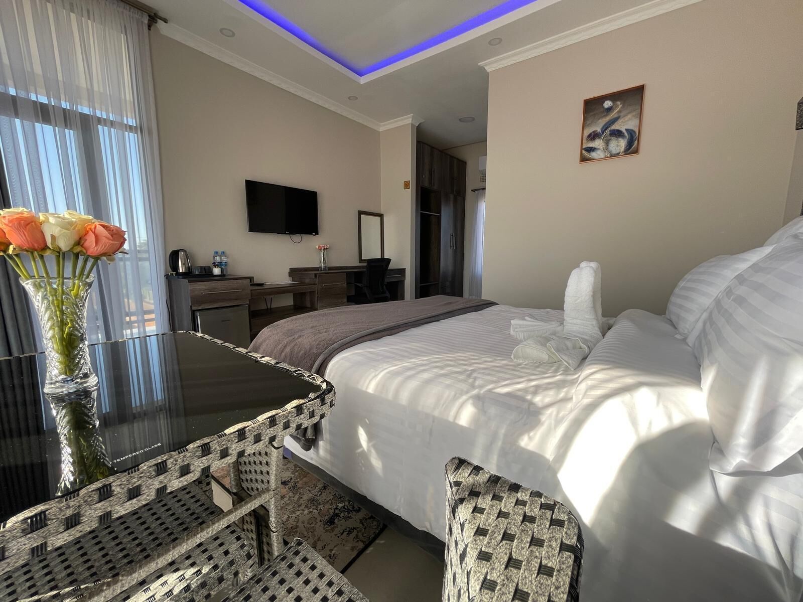 A hotel room with a bed, a desk, a chair, a TV, and a painting on the wall.