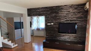 Un salon moderne avec un plancher en bois, un escalier, un téléviseur à écran plat fixé à un mur texturé et un canapé rouge.